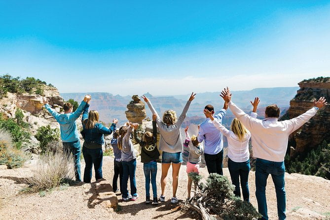 Group of people holding arms in the air at the edge of a cliff looking over mountains