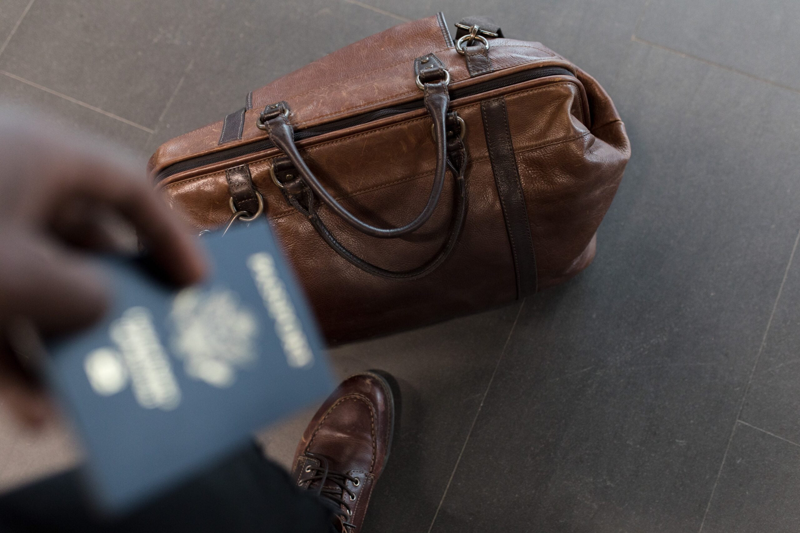Man holding passport standing next to travel bag